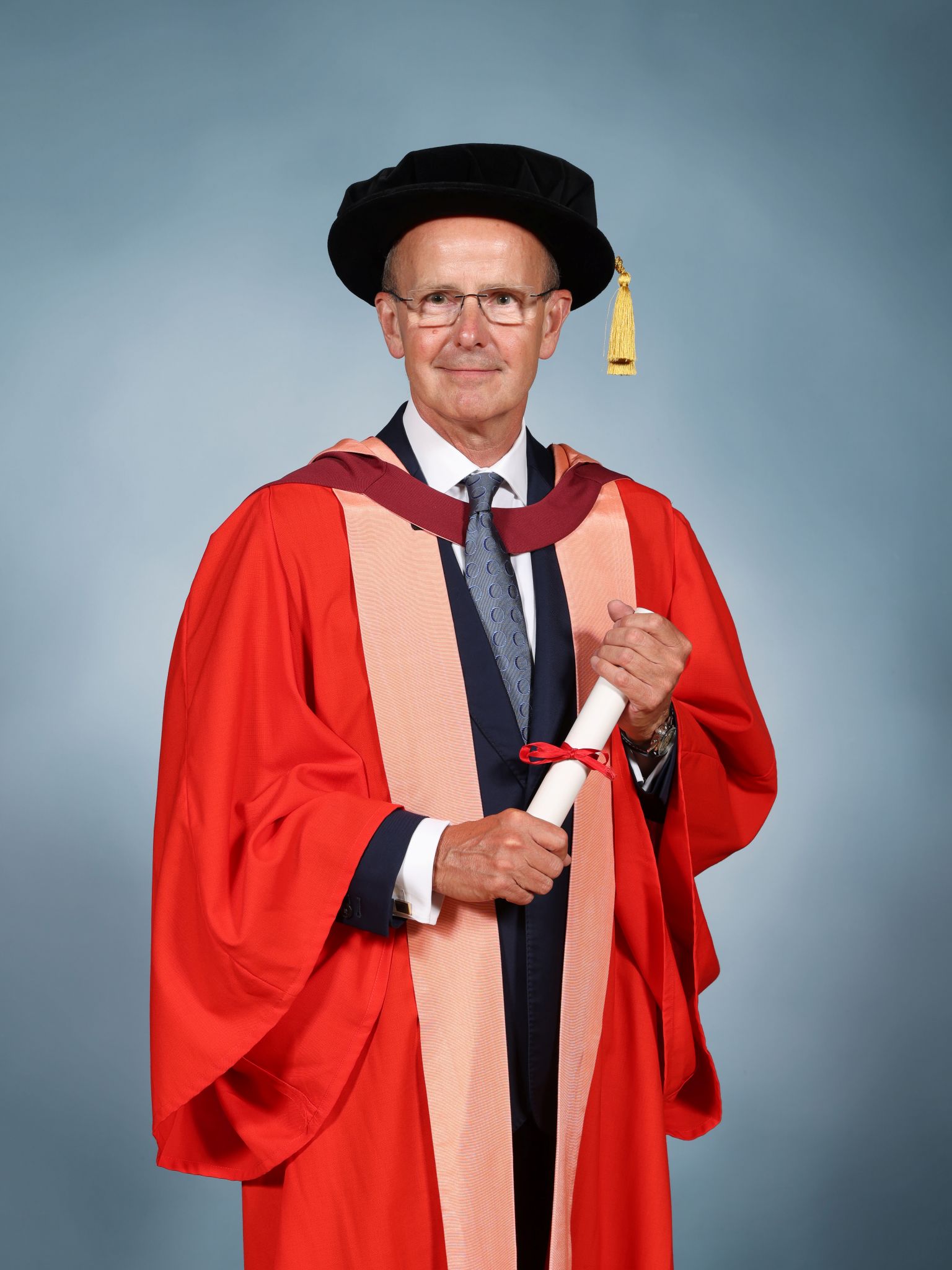 Sir Jeremy Fleming wearing a mortar board and holding a parchment